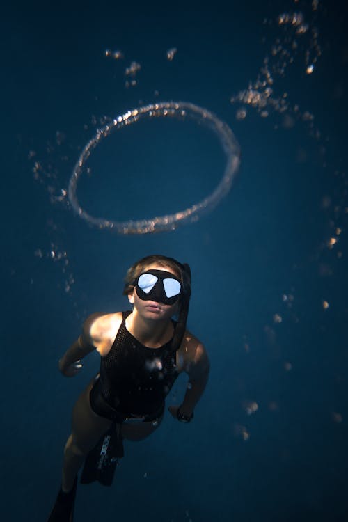 Free Woman in Black Goggles and Black Swimsuit Floating Up to Bubble Ring Stock Photo