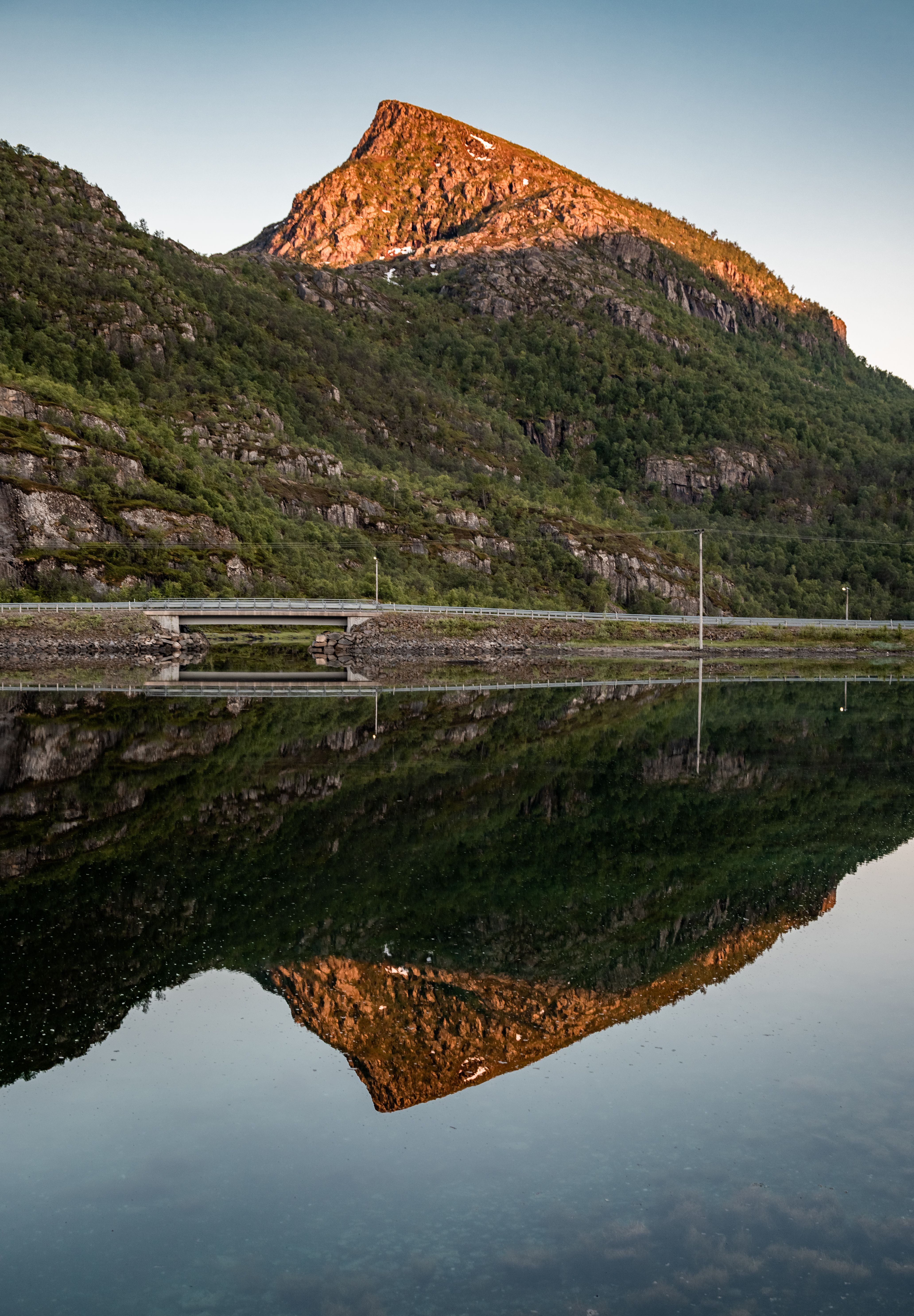 Golden hour view of a mountain reflecting in a tranquil fjord in Digermulen, Nordland, Norge.