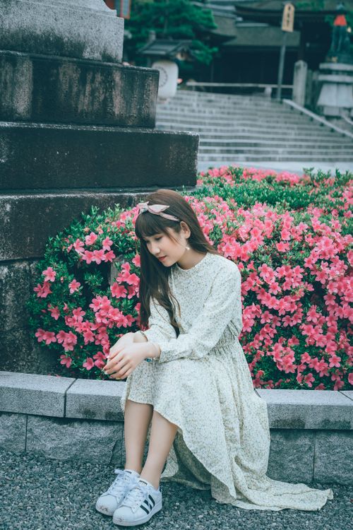Free A young woman sitting by bright pink flowers, deep in thought, next to stone steps. Stock Photo