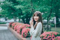 一位长发女子在绿意盎然的公园里，手持一朵粉花，灿烂地微笑着