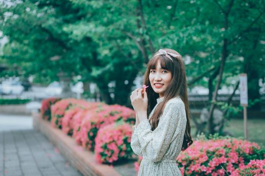 一位长发女子在绿意盎然的公园里，手持一朵粉花，灿烂地微笑着