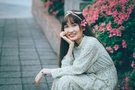 一位身着花裙的女子肖像，被盛开的粉红色花朵环绕，显得快乐而宁静