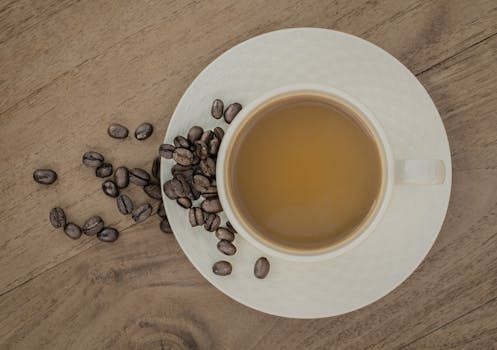 Top view of a coffee cup with scattered beans on a wooden surface.