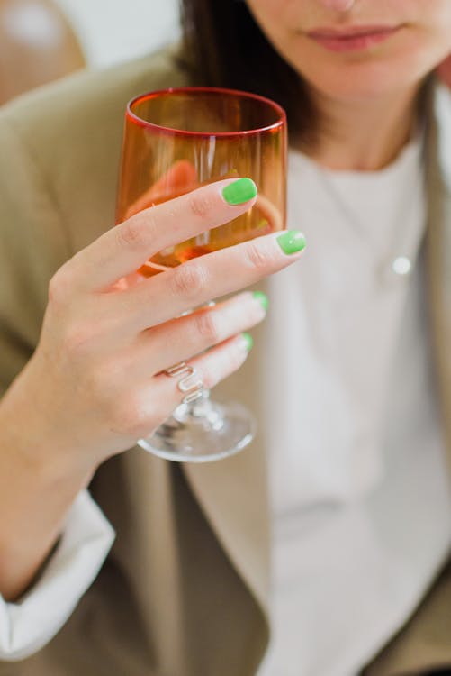 Crop unrecognizable stylish female with green manicure and colorful glass of champagne in daylight