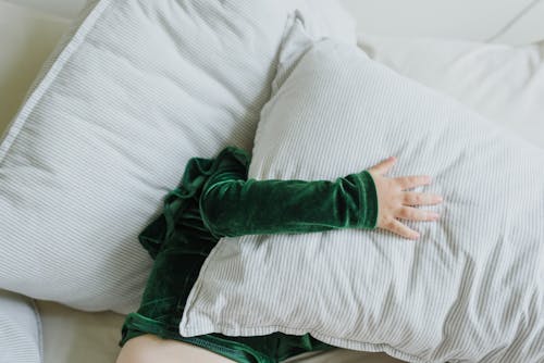 Free Top view of anonymous little kid in plush hoodie lying on soft bed and covering face with pillow Stock Photo