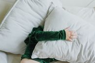 Top view of anonymous little kid in plush hoodie lying on soft bed and covering face with pillow