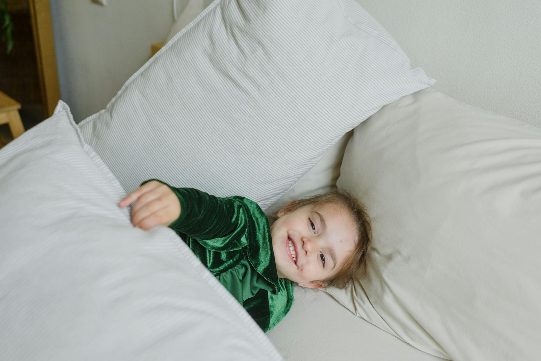 Image of a cheerful little kid laying on comfortable bed and smiling