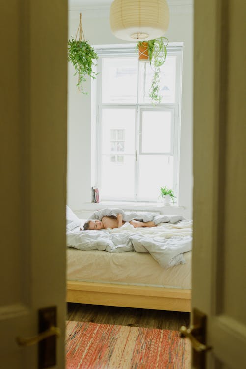 Free Anonymous kid resting under blanket on bed in modern apartment Stock Photo