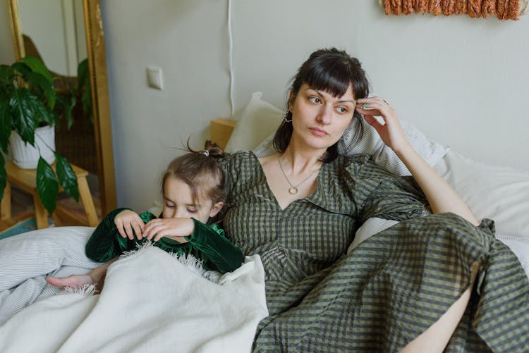 Tired Mother With Cute Daughter Resting On Bed In Cozy Room