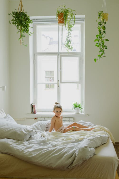 Curious little girl relaxing on soft bed in daylight