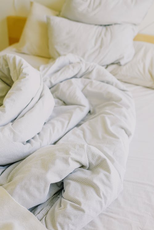 Free From above of comfortable messy with soft white blanket and pillows in sunny morning Stock Photo