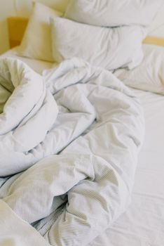 在阳光明媚的早晨，上面是舒适的凌乱与柔软的白色毯子和枕头