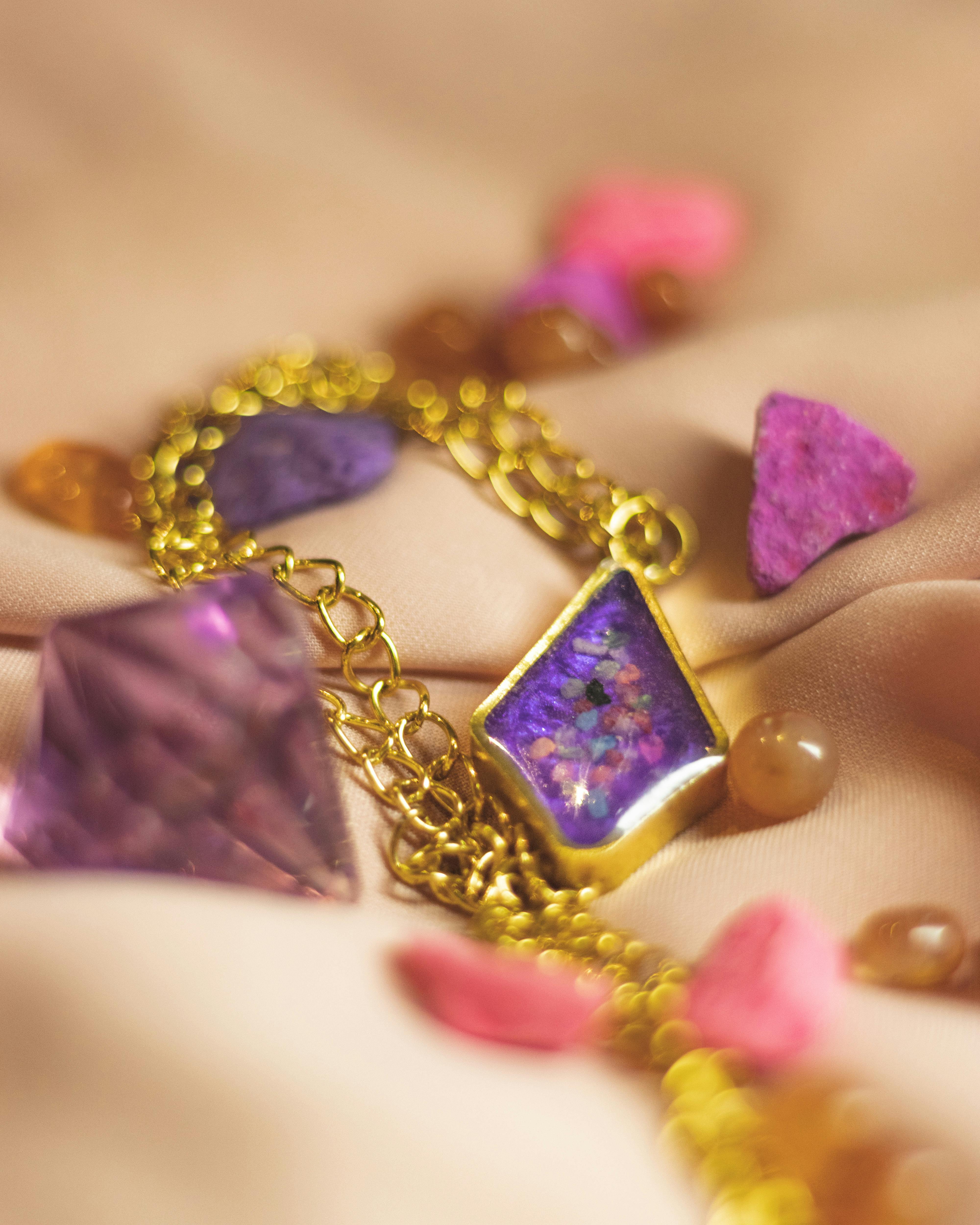Close-up of a golden bracelet with purple and pink gemstones on a soft fabric background.