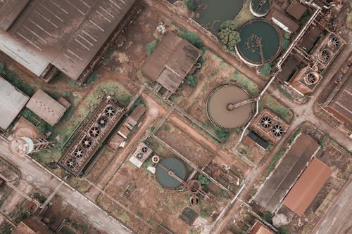 Free Drone view of shabby factory with round settling tanks with mechanical means removing solids in water treatment plant Stock Photo