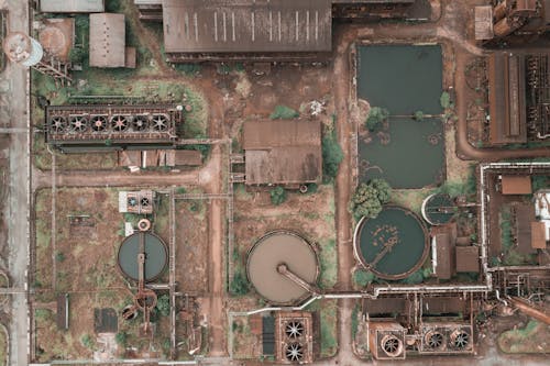 Drone view of abandoned chemical plant with rusty and unused production buildings and round tanks with dirty water