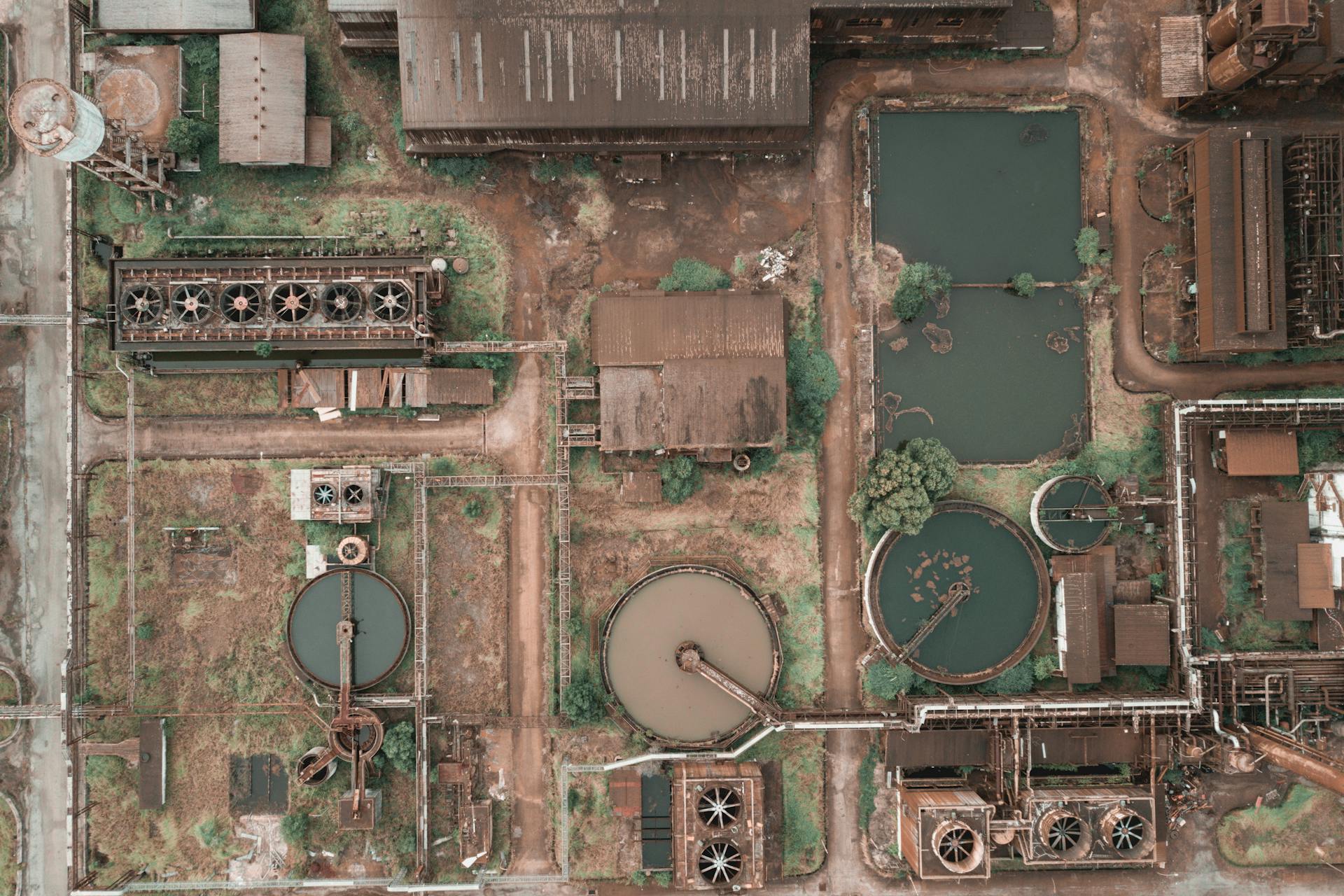 Drone view of abandoned chemical plant with rusty and unused production buildings and round tanks with dirty water