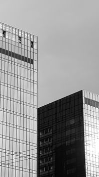 Black and white photo of modern skyscrapers with reflective glass facade against a cloudy sky.