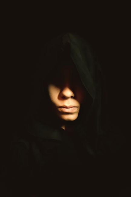 A shadowy figure with a hood obscures their face, creating an aura of mystery and intrigue.
