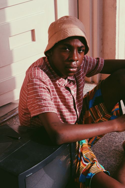 Free Young African American man in casual clothes and bucket hat sitting on floor near old TV and looking at camera Stock Photo
