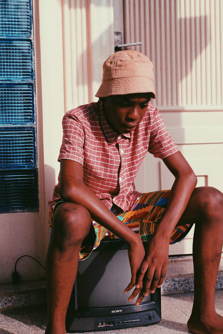 Black Young Man Sitting On Old TV And Looking Down