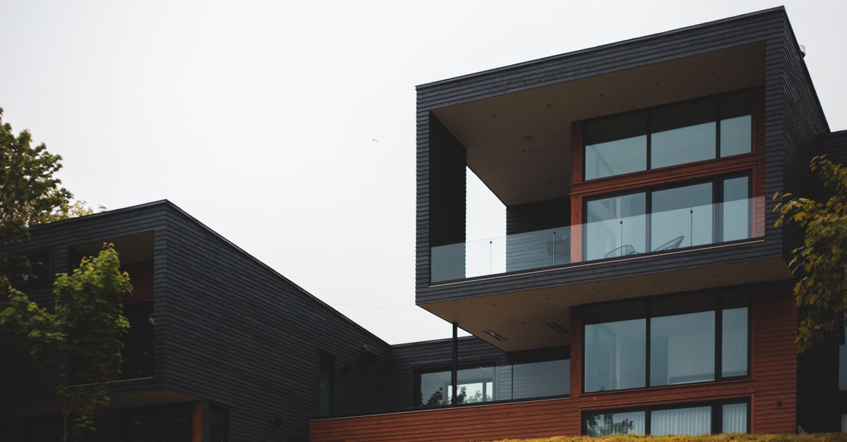 From below of contemporary geometric building with big windows and stylish design of balcony on green grass with trees
