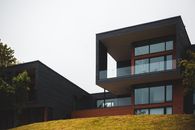 From below of contemporary geometric building with big windows and stylish design of balcony on green grass with trees