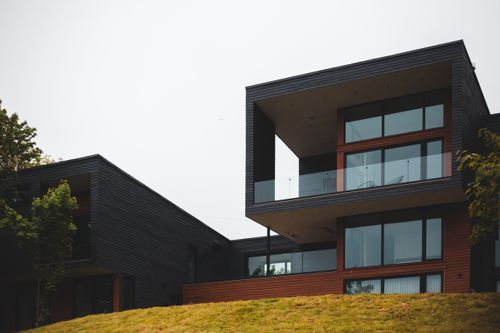 Free From below of contemporary geometric building with big windows and stylish design of balcony on green grass with trees Stock Photo