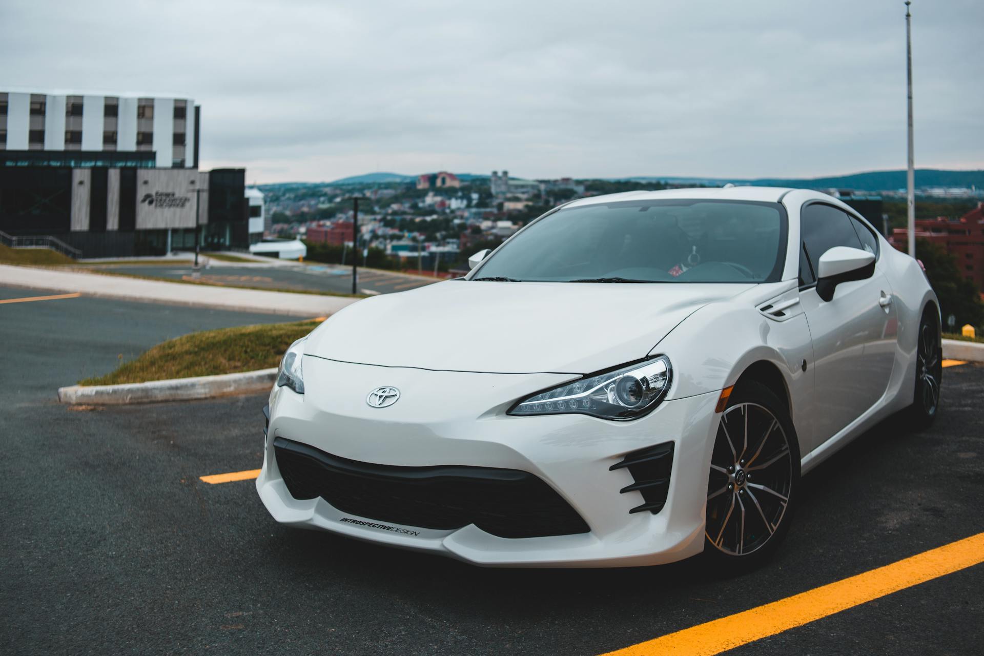 Contemporary luxuty vehicle parked on asphalt road near yellow marking lines against overcast sky with settlement on background in city