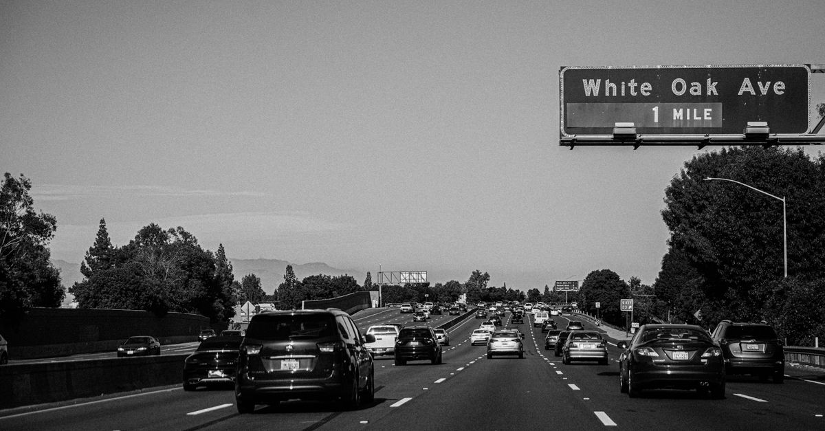 Busy Los Angeles highway scene in grayscale, featuring vehicles and road signs.