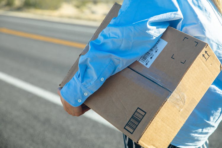 Person Carrying A Brown Box On A Road