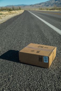 一条长长的空荡道路延伸至沙漠深处，路中间放着一个纸板箱