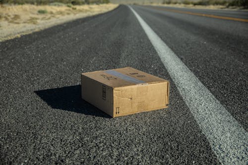 Free Brown Cardboard Box on Gray Asphalt Road Stock Photo