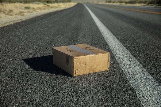 空旷的沙漠道路上，一个纸板箱被放置在明亮的阳光下