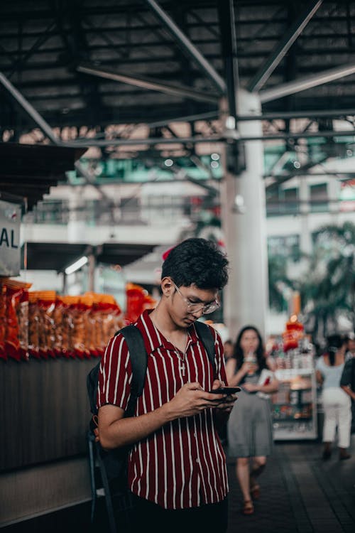 A Man in a Striped Shirt Texting on His Smartphone