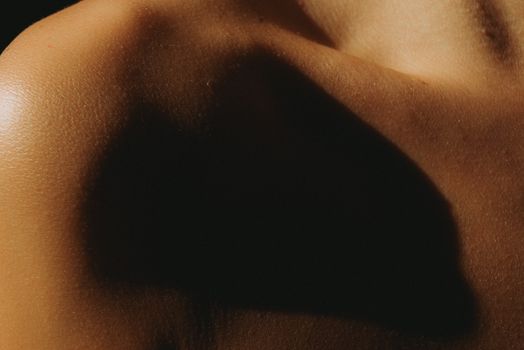 Close-up artistic photo highlighting shadows on bare shoulder. Captivating lighting effect creates a dramatic mood.