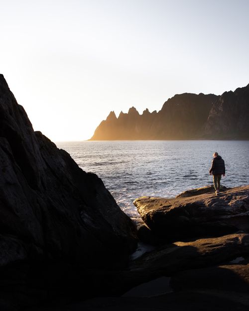 Free Person walking by ocean cliffs at sunset, capturing Norway's scenic beauty. Stock Photo