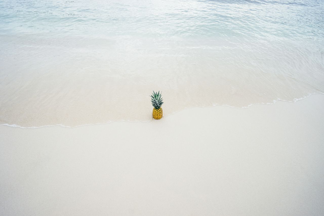 a vibrant pineapple rests on the sandy beach with gentle waves approac