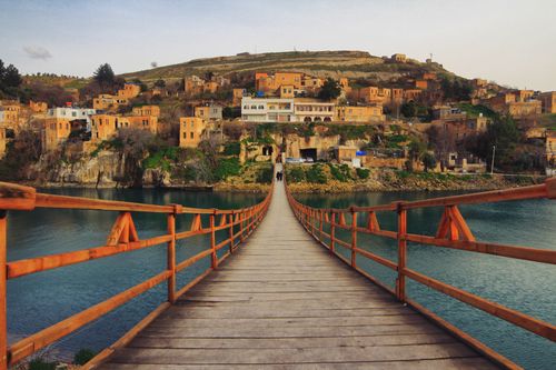 Free A picturesque wooden bridge leading to a historic town in Şanlıurfa, Turkey, over a serene river. Stock Photo
