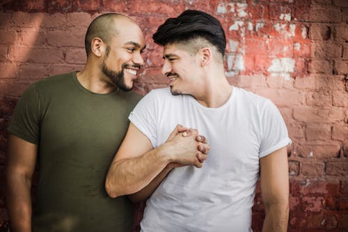 Free Men Holding Hands While Standing in Front of a Brick Wall Stock Photo