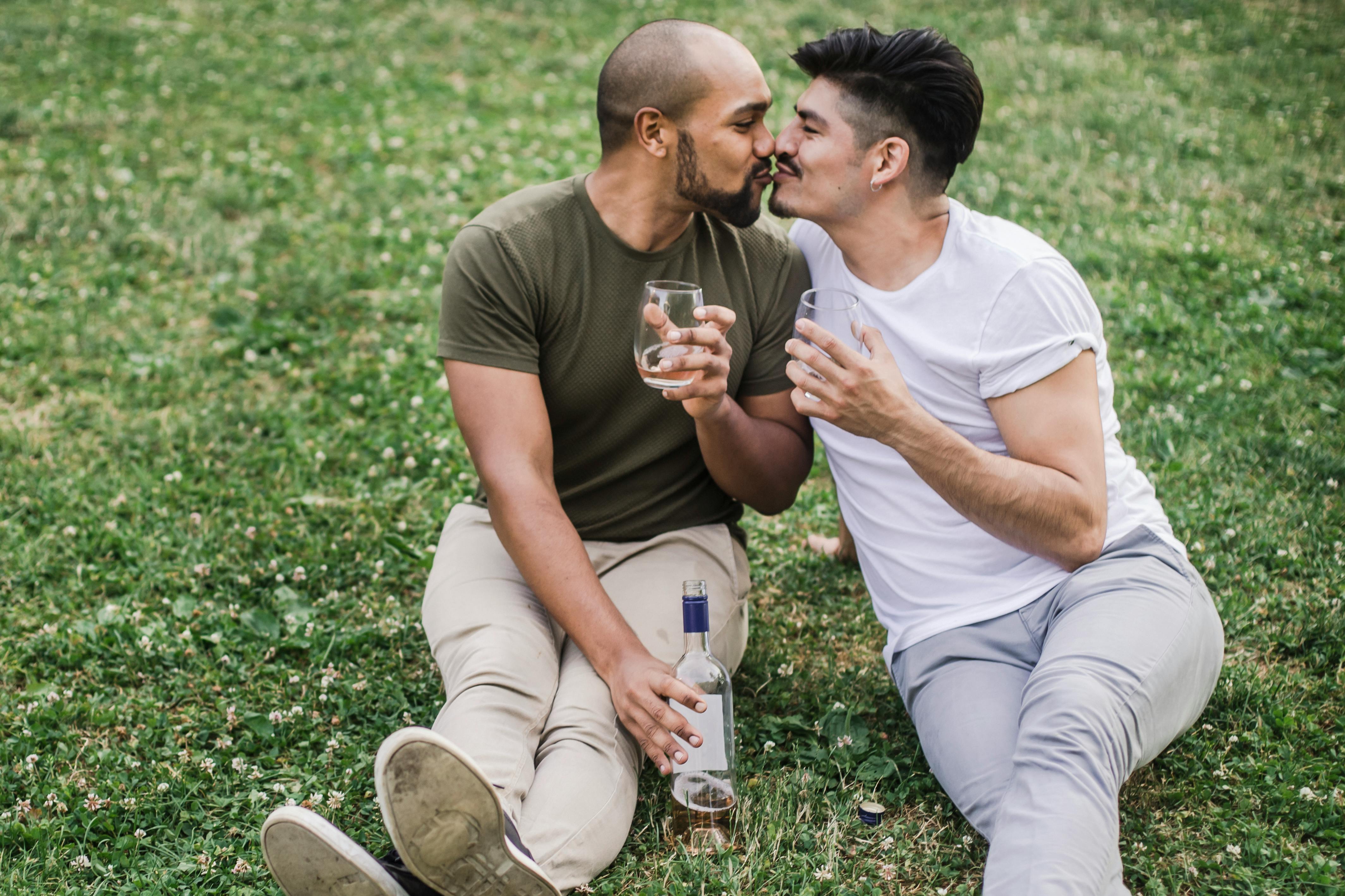 two men kissing and sitting on the grass