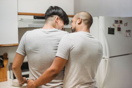 Free Two men embracing in a kitchen, sharing an intimate moment at home. Stock Photo