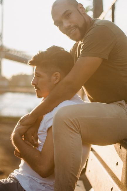 A loving interracial gay couple embracing on a park bench during a beautiful sunset.