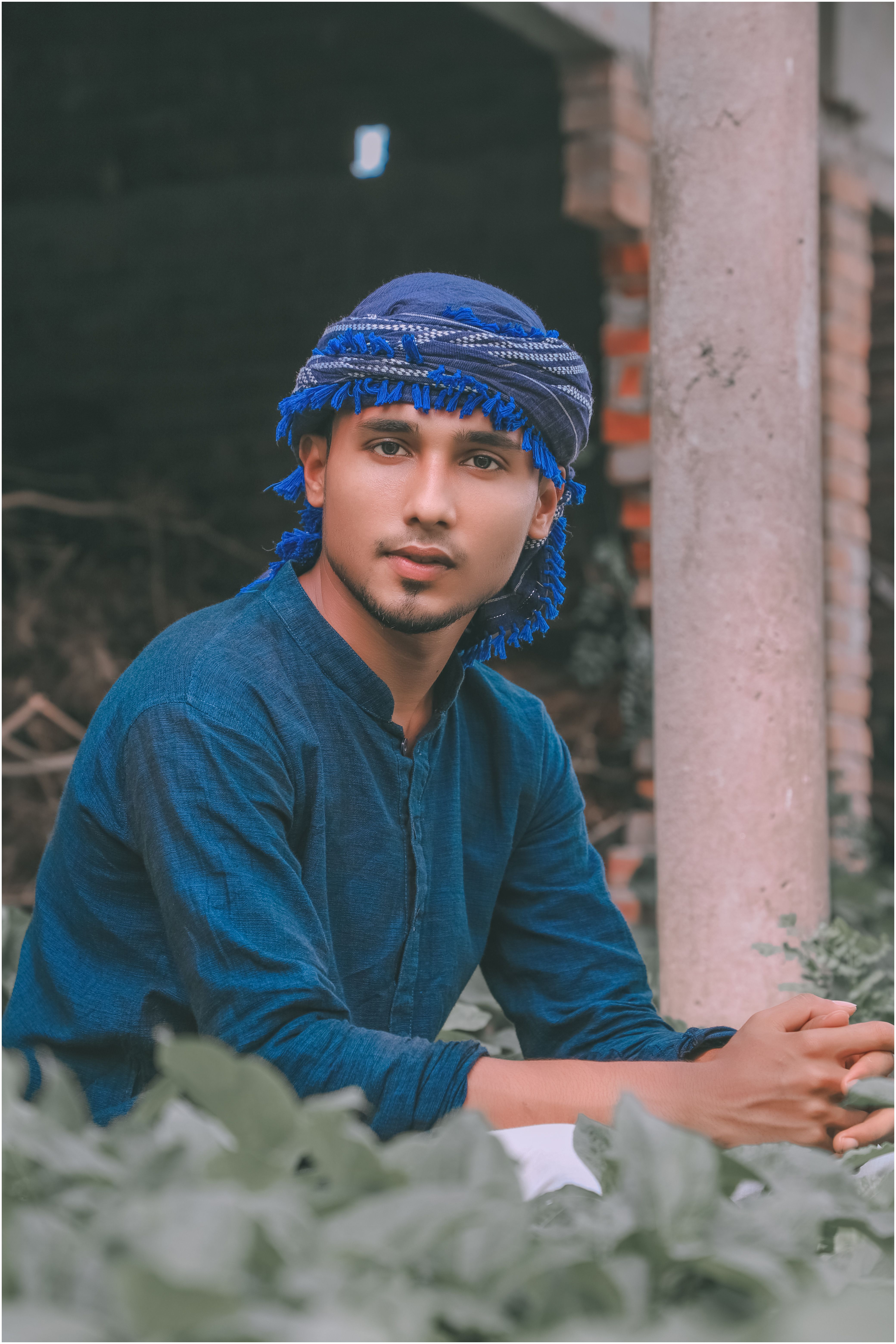 A young man wearing a blue headscarf, sitting indoors in natural light.