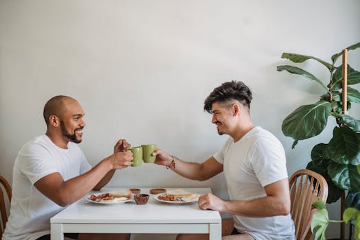 Two men toast with coffee mugs during a home breakfast setting.