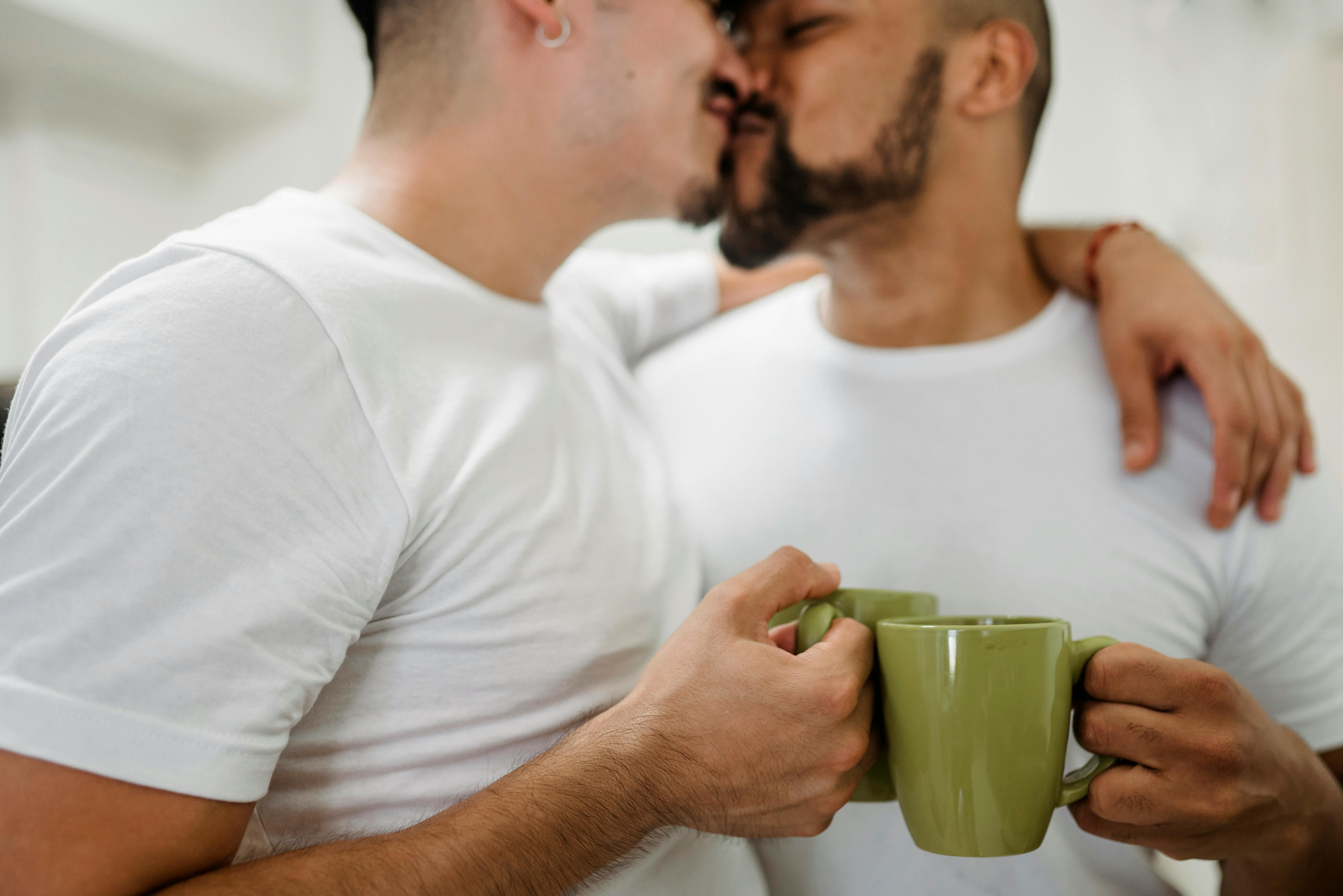 two men holding cups and kissing