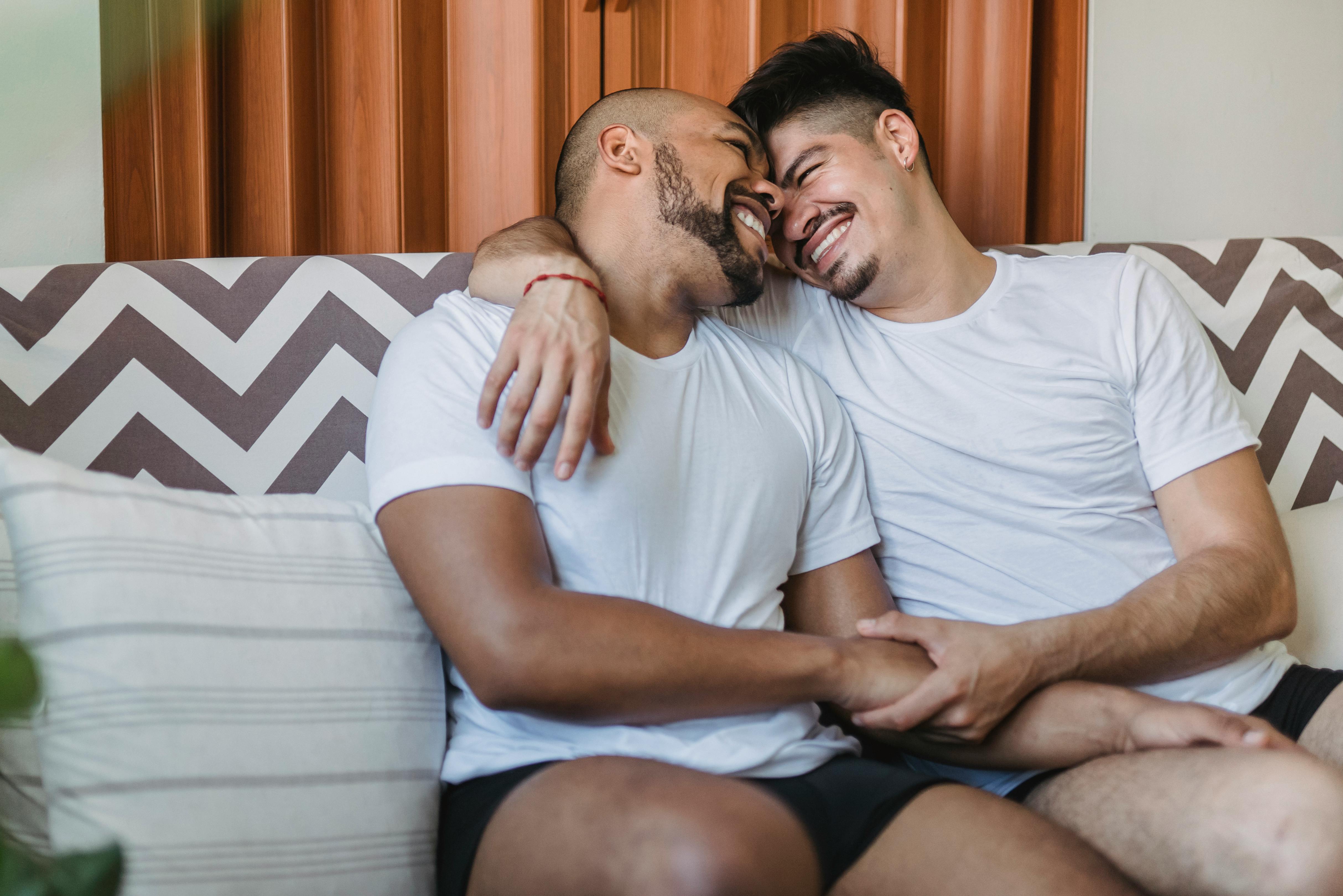 A joyful gay couple cuddling and smiling on a couch, showcasing affection and happiness