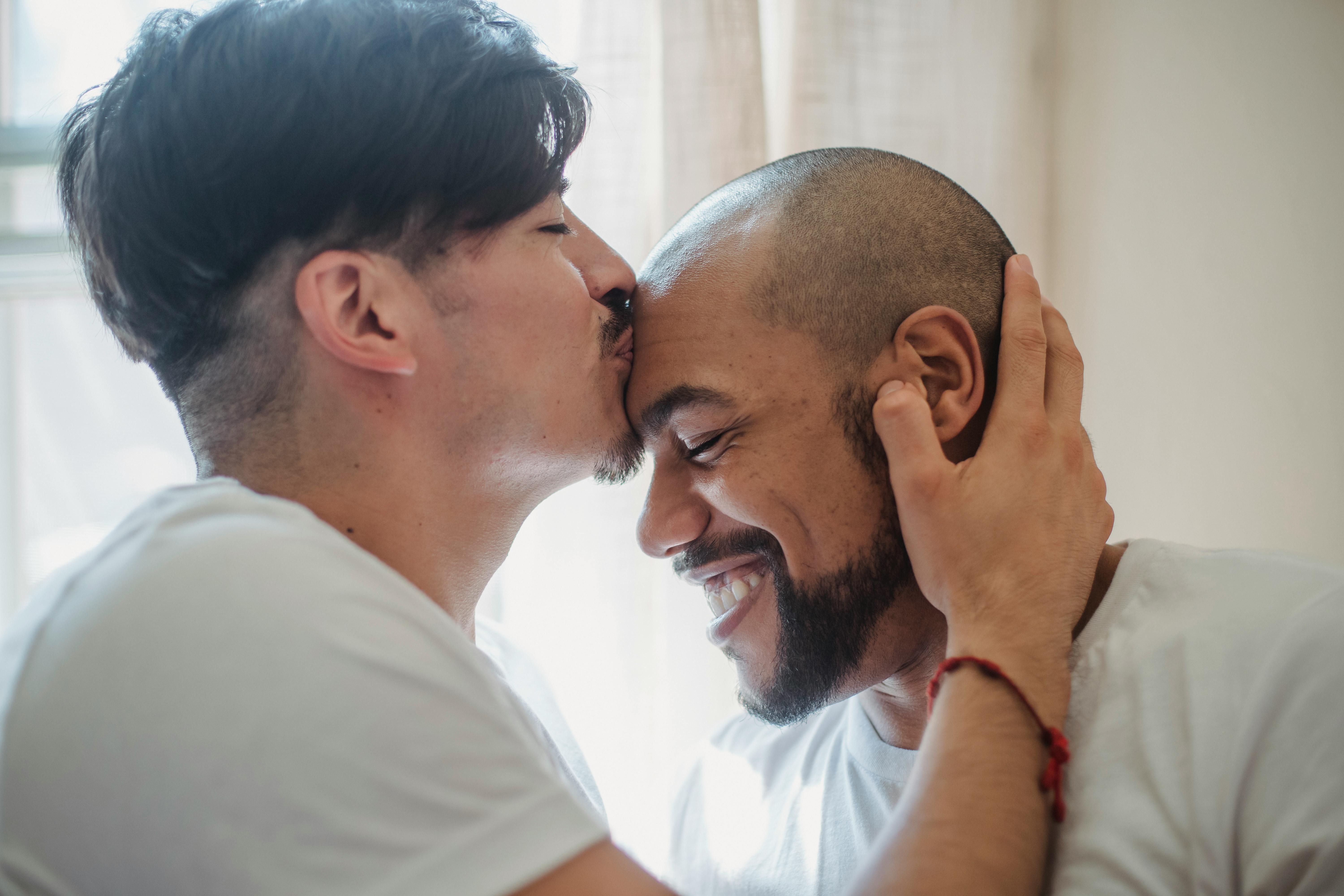 man kissing another man on the forehead