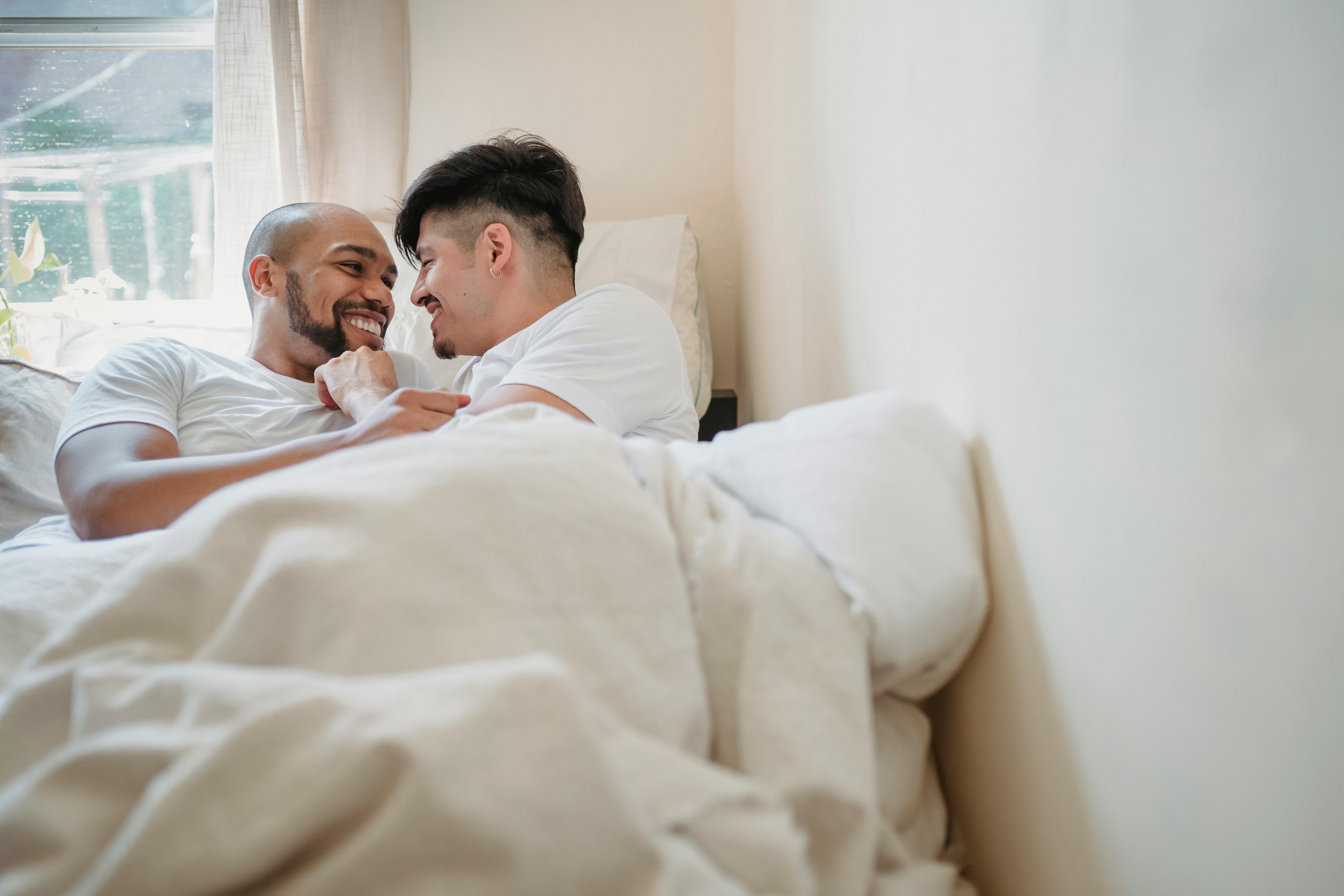 two men smiling in bed together