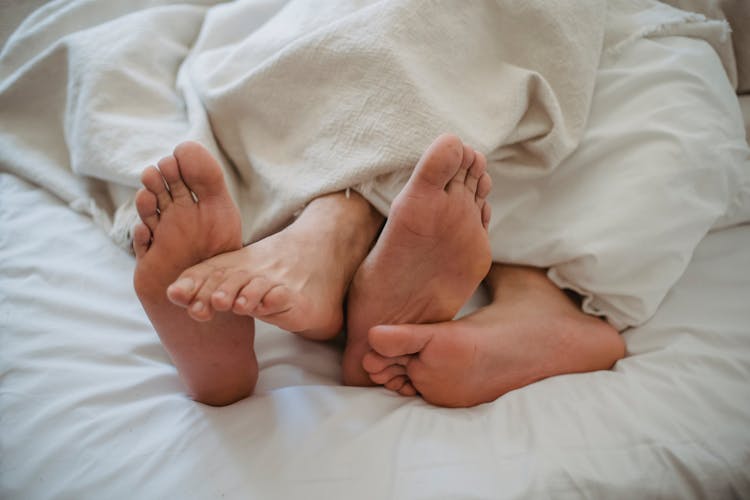 Close-up Of Mens Feet Intertwined In Bed 