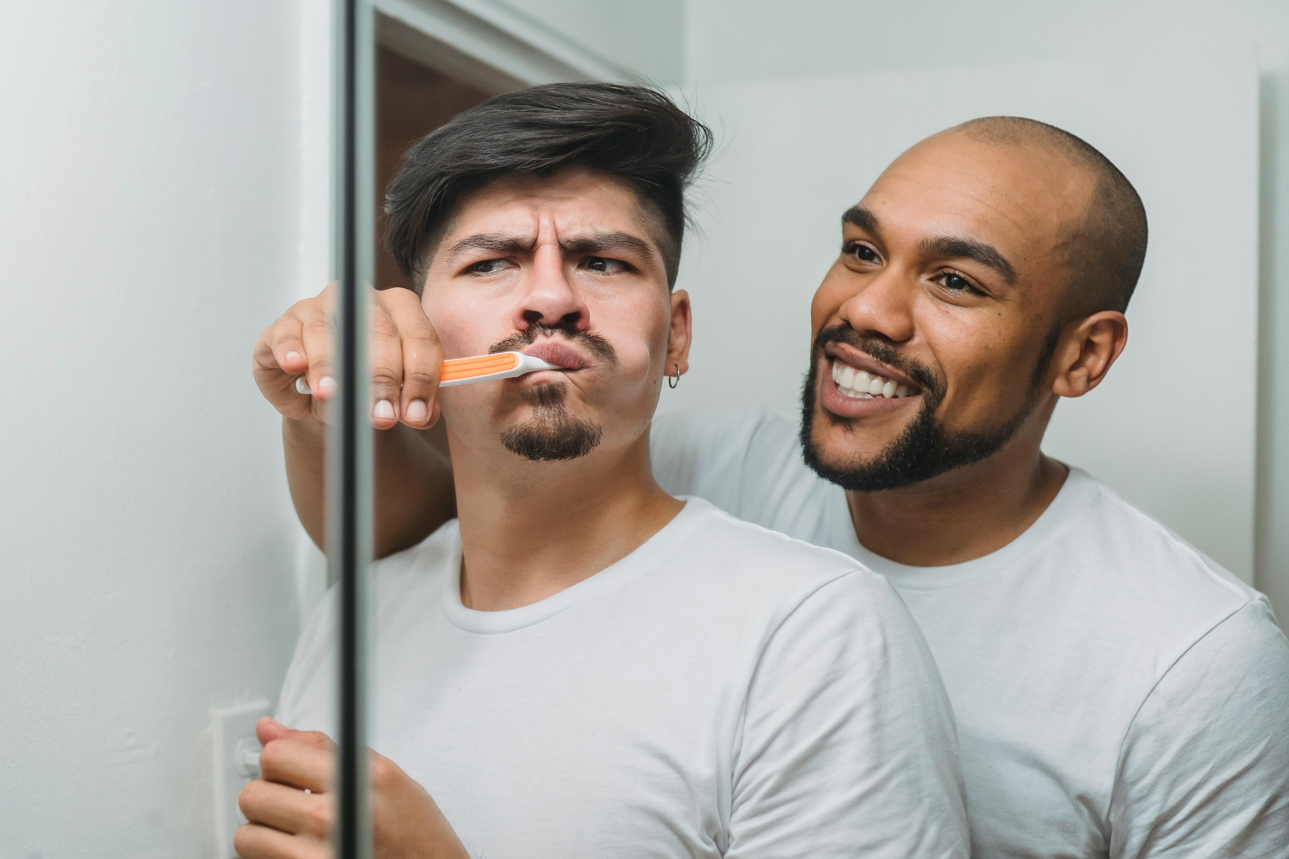 a man in white crew neck shirt brushing the teeth of a man in white crew neck shirt